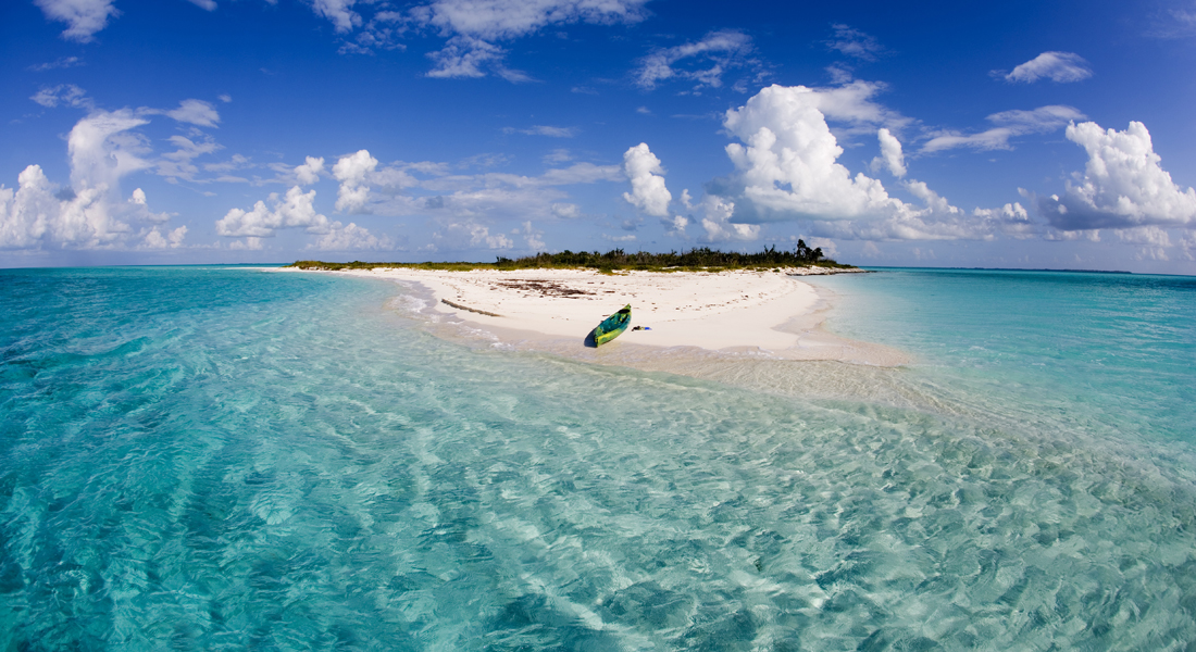 A kayak docked on a beach with blue sky above the island