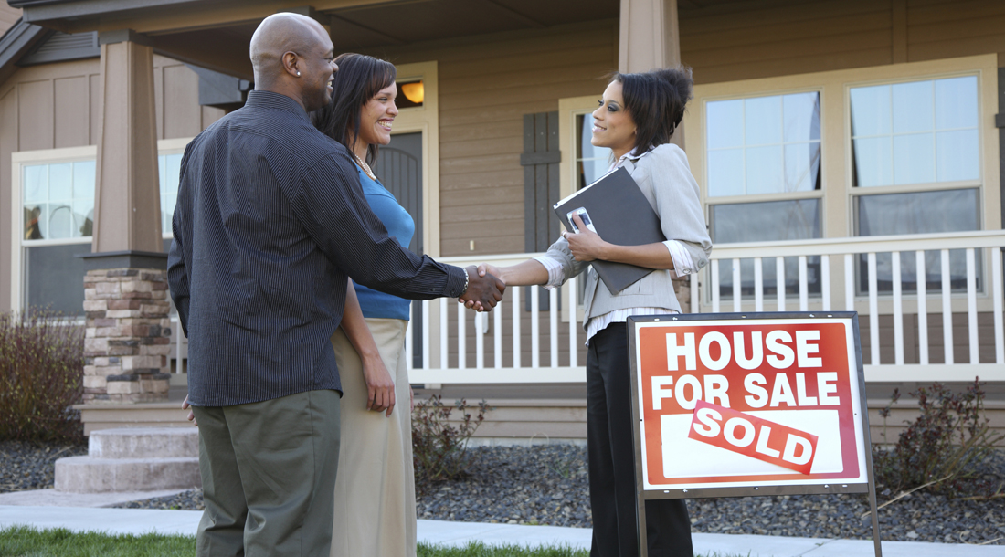 Couple shakes hands with realator in fron of new home